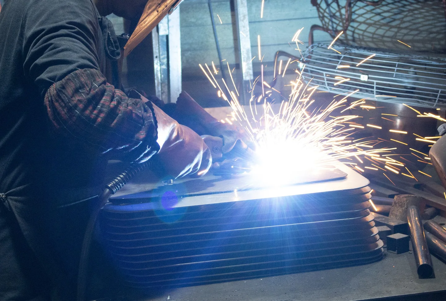 Worker welding metal parts at a workstation with bright sparks